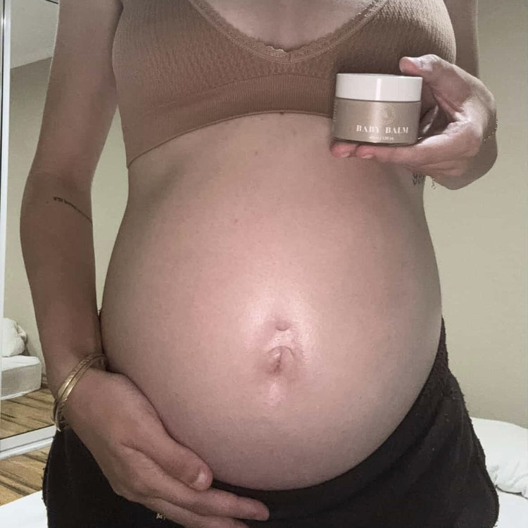 Pregnant mum with a moisturised belly holding a jar of our Organic Baby Balm.