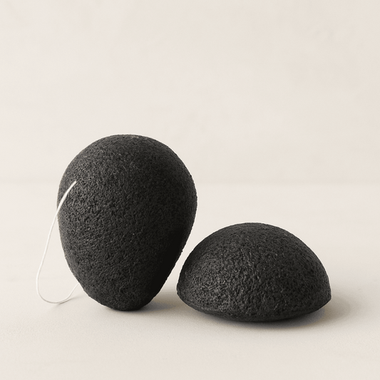 Two charcoal infused konjac sponges on display on a neutral background.