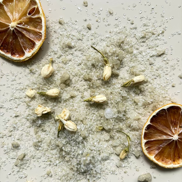 Dried lemons, dried jasmine flowers and 'restore' magnesium bath salts content on a neutral coloured surface.