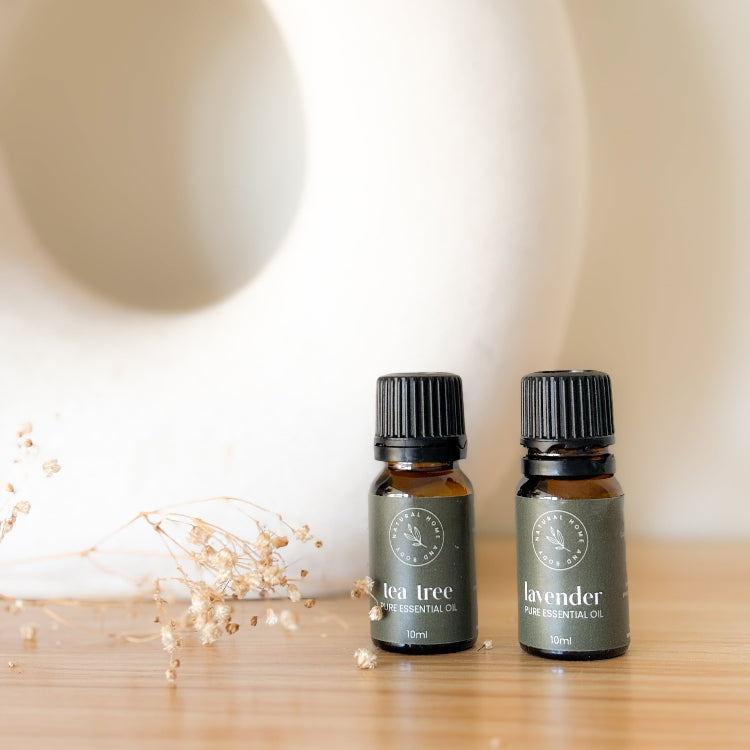 Two essential oil bottles labeled 'Tea Tree' and 'Lavender' on a wooden surface with a neutral background.