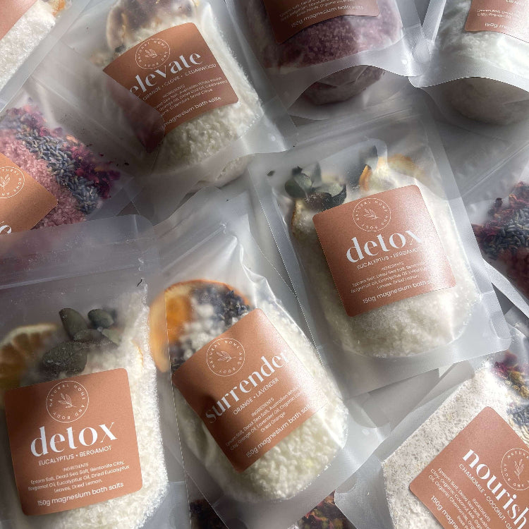 Packaged magnesium bath salts with 'detox', 'surrender', and 'nourish' labels on a neutral background.
