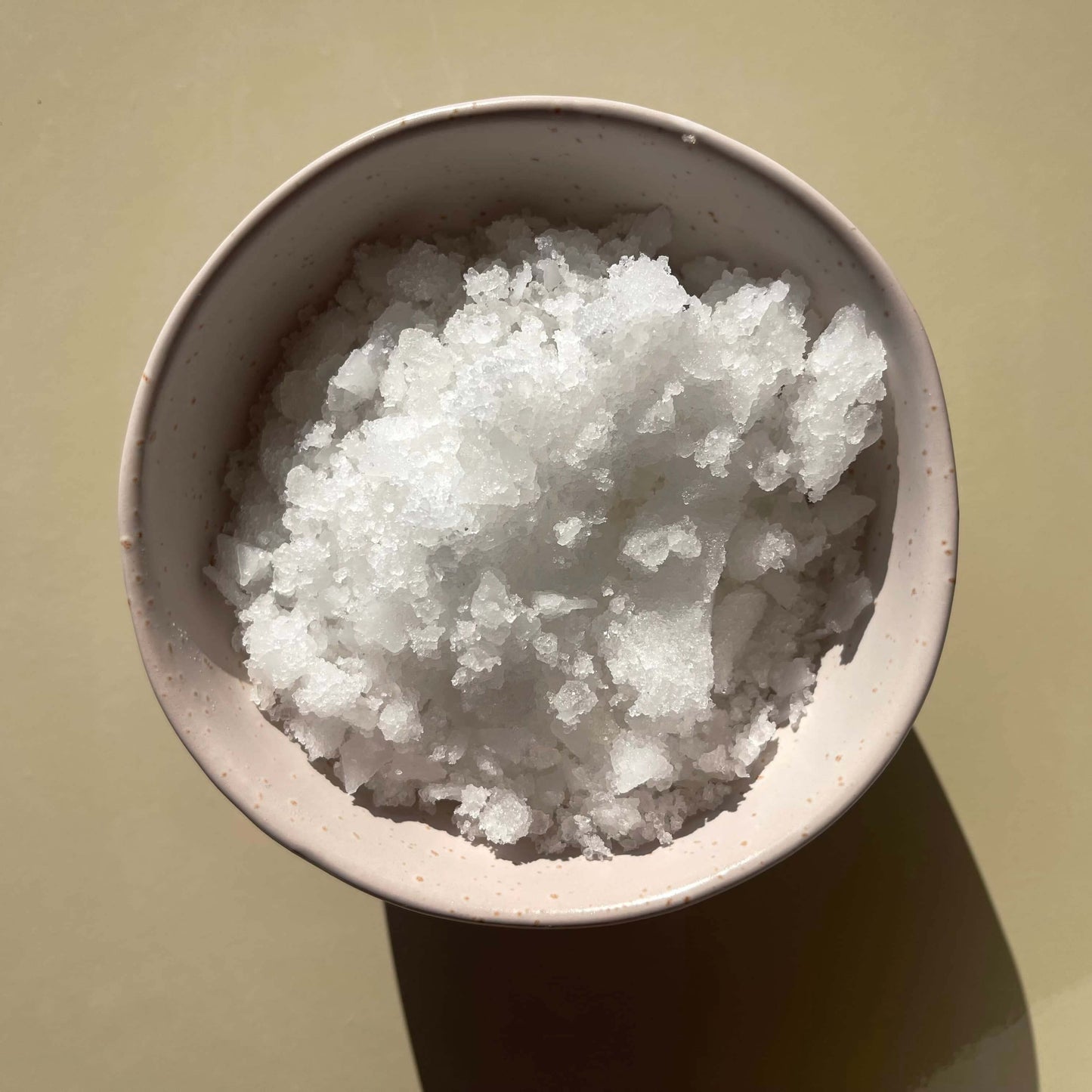 Magnesium bath salts product displayed in a bowl, on a beige background to show the texture of the salts.