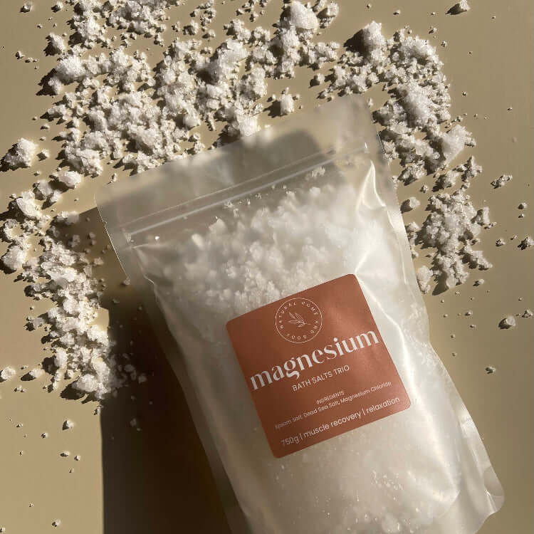 Magnesium bath salts, on a beige background with salts scattered around the product to showcase the look/texture.