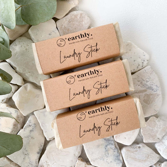 Three natural laundry sticks placed on a styled background of white pebbled rocks and some dried eucalyptus leaves.