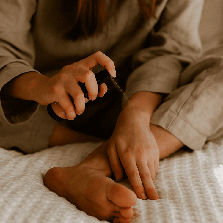 Woman spraying a topical magnesium oil onto her feet while relaxing on a cosy bed.