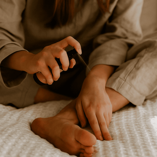 Woman spraying a topical magnesium oil onto her feet while relaxing on a cosy bed.
