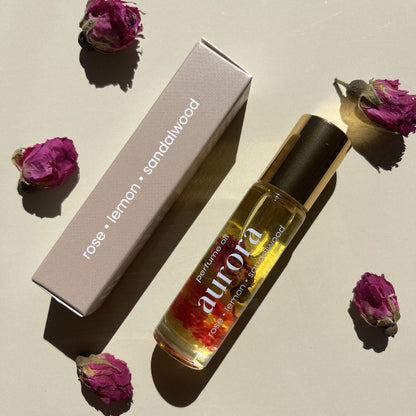 Aurora perfume oil glass bottle and boxed packaging with dried flowers on a neutral background.