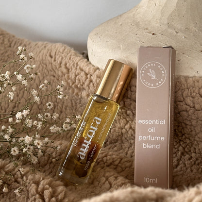 Aurora essential oil perfume blend bottle and box on a textured surface with flowers.