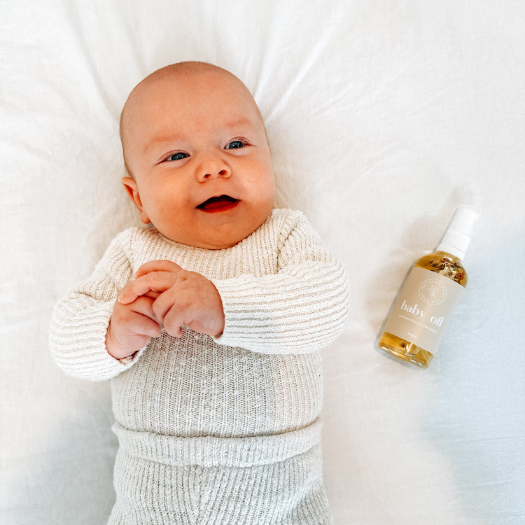 Baby lying on a white blanket with a bottle of baby oil next to it