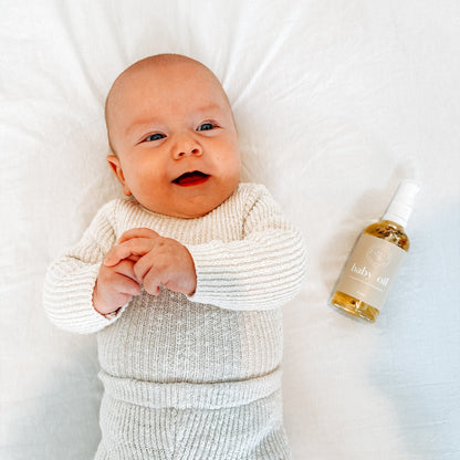Baby lying on a white blanket with a bottle of baby oil next to it