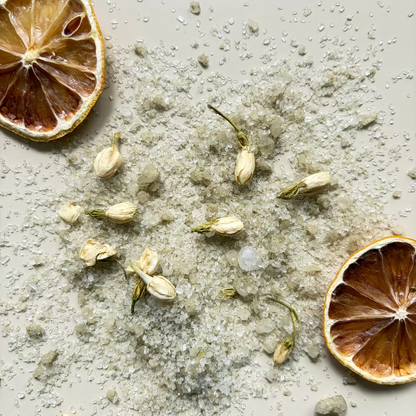 Dried lemons, dried jasmine flowers and 'restore' magnesium bath salts content on a neutral coloured surface.