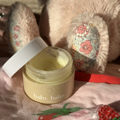 Baby balm surrounded by baby girl pink items.