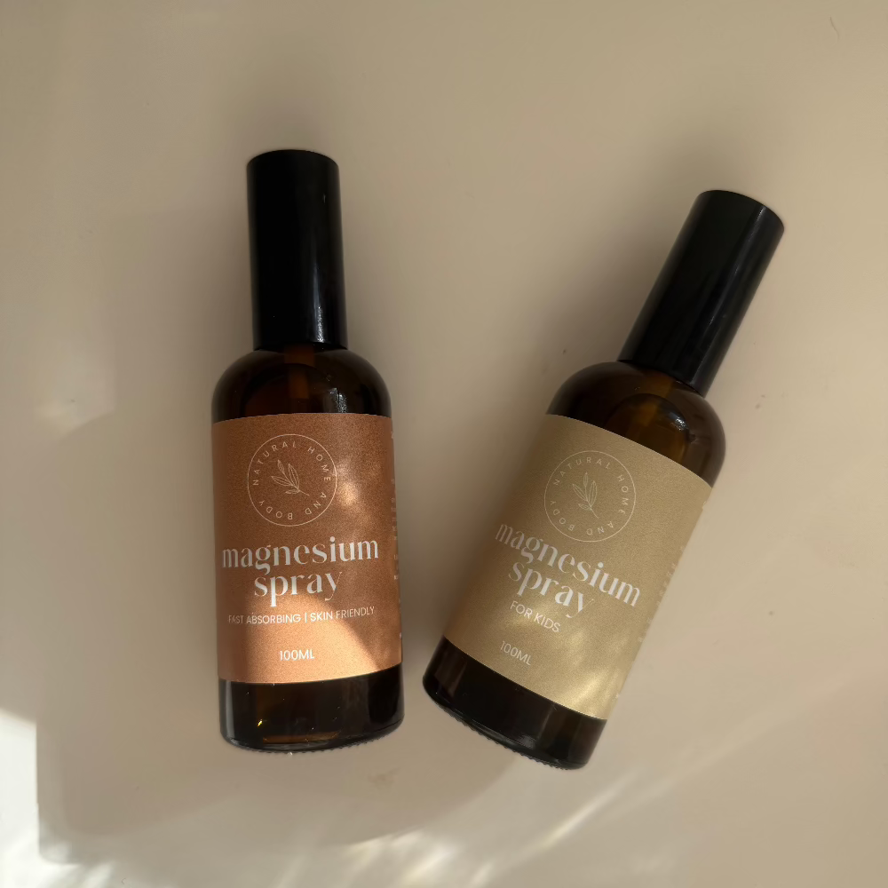 Two magnesium oil sprays, with a beige and dusty orange label on a white desk. Birds eye view with the sun shining on the products.